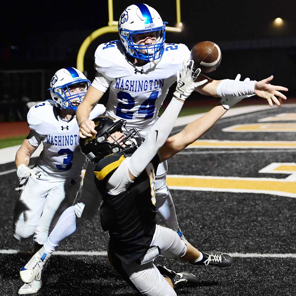 A football player in black reaches to catch a pass in the end zone as two Washington defenders close in, capturing a moment of intensity worthy of any Premier Media Network highlight.