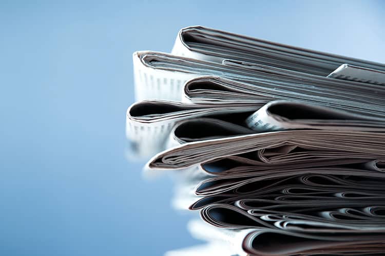 A close-up view of a stack of folded newspapers against a blue background highlights the enduring appeal of print advertising in today’s media mix.