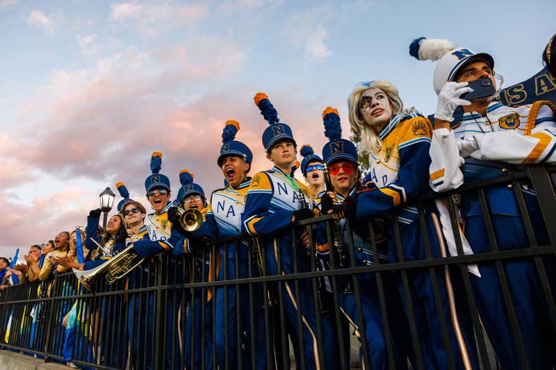 The band stands behind a fence, holding their instruments, ready to perform.