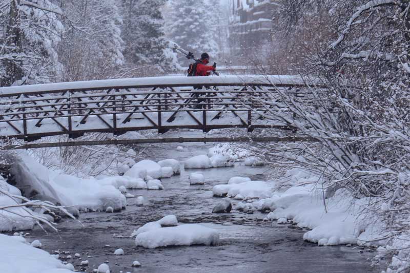 A person walks across a snow-covered bridge, surrounded by a serene winter landscape.