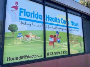 Window display for Florida Health Care News featuring a flamingo, houses, text about health care professionals, and contact info—now highlighting our expertise in Programmatic Advertising. Visit our website or call today!.