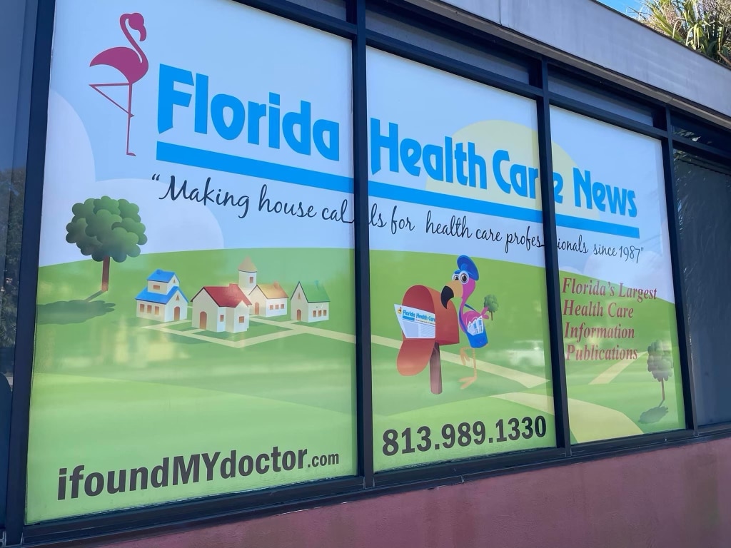 Window display for Florida Health Care News featuring a flamingo, houses, text about health care professionals, and contact info—now highlighting our expertise in Programmatic Advertising. Visit our website or call today!.