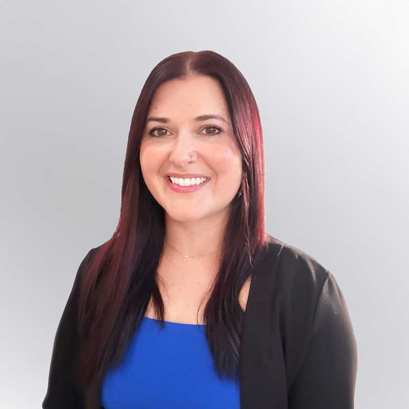 Woman with long dark hair wearing a black blazer over a blue top, smiling at the camera with a light gray background, representing Premier Media Network’s expertise in digital & advertising solutions.