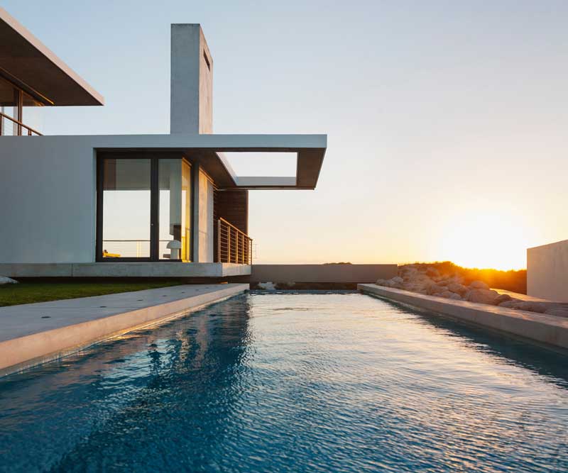 Modern house with large windows and a cantilevered roof beside a narrow swimming pool at sunset, showcasing stunning design that rivals the innovation seen in Premier Media Network's digital & advertising solutions.
