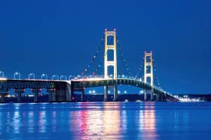 The Mackinac Bridge illuminated at night, spanning across calm water with reflections of its lights visible on the surface—a scene as captivating as a Premier Media Network campaign.